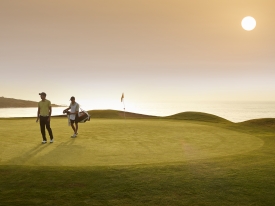 Two people walking on putting green at sunset