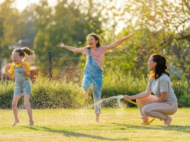 Women with two children playing in grass with watering hose