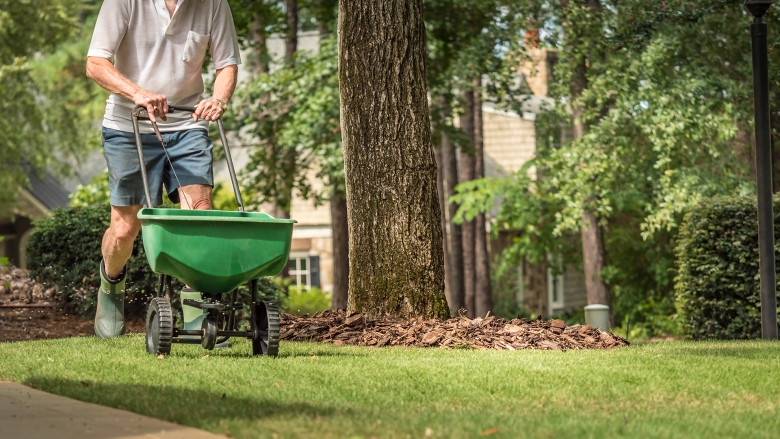 Man with seed spreader on wheels with trees in the background