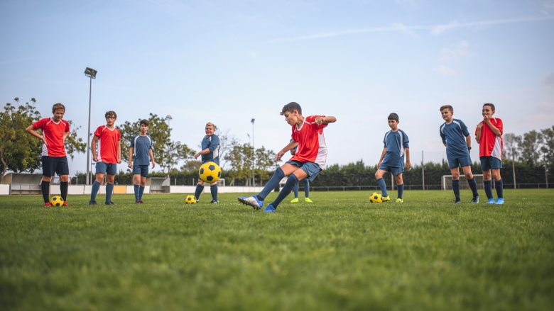 Young soccer players in red and blue jerseys kicking yellow and black soccer balls