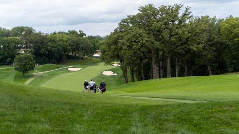 Photo of a golf course with three players and trees in the distance 