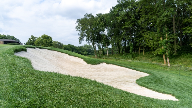 A sand golf course bunker with trees and cloudy sky in the background