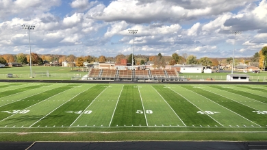 Football field with lines and numbers facing a small set of bleachers with trees and sky in the background