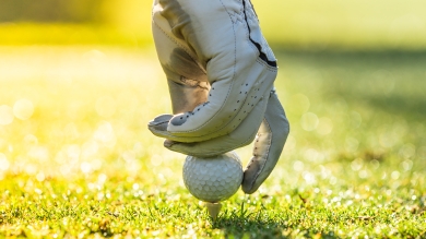 Gloved hand places golf ball on tee in grass 