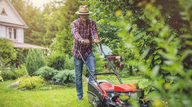 Man in a hat mowing lawn with red lawn mower and house in the background