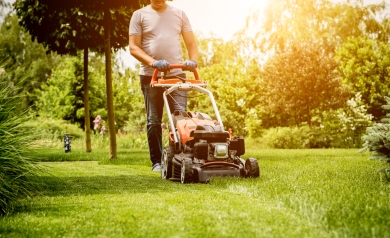 Man in grey shirt pushes red lawn mower over green grass in a residential yard