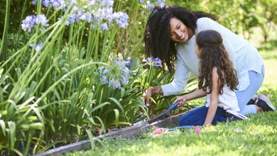 Mother and daughter working on flowers in the garden while sitting on green grass
