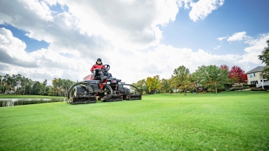 Man mowing fairway with professional mower under cloudy sky.