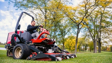 Man mowing grass under trees on professional lawn mower.
