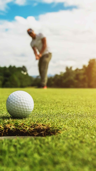 Man putting white golf ball on putting green under cloudy sky.