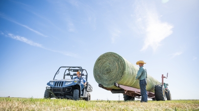 Farmer stands next to hay bales on a trailer 