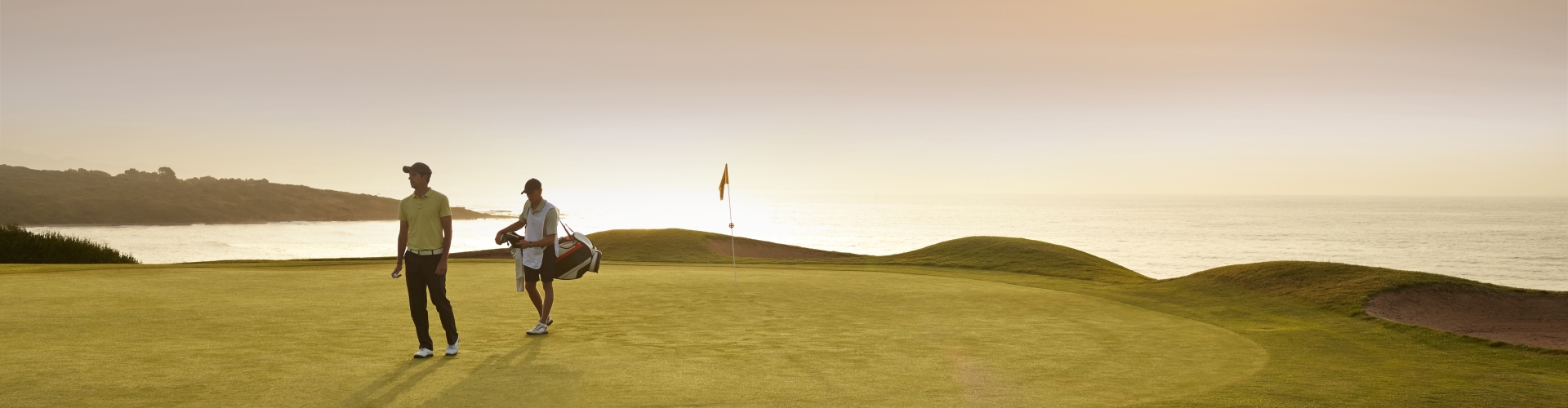 Two people walking on putting green at sunset