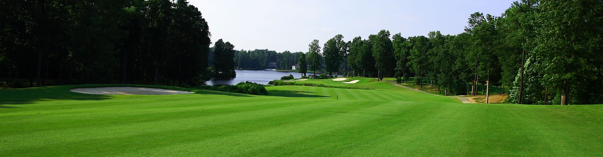 Green golf course fairway under blue skies with evergreen trees lining the course.