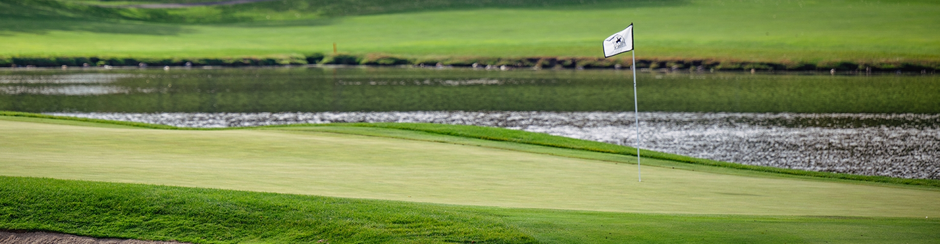 Golf hole with flag, green grass and water 