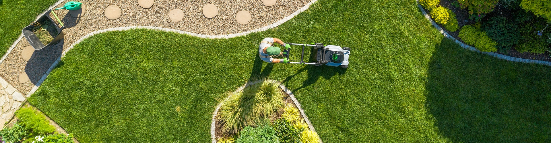 Overhead view of landscaper mowing a yard with grass, bushes, and path