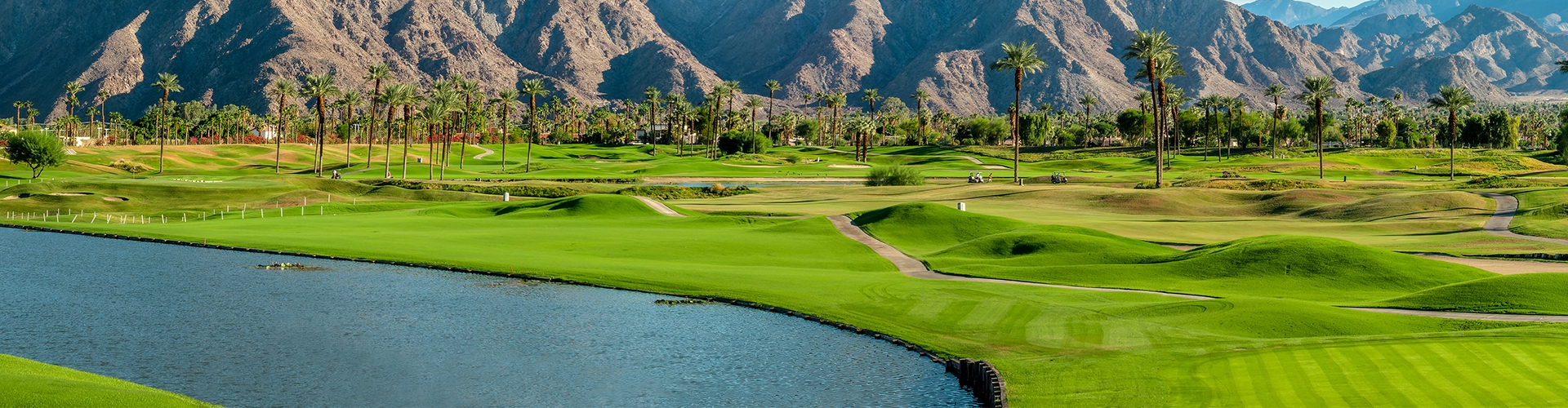 Golf course with green grass, palm trees, cliffs in background