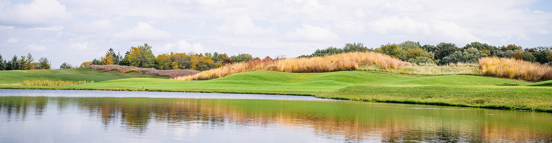 Landscape of green golf course turf with clouds and blue sky in background