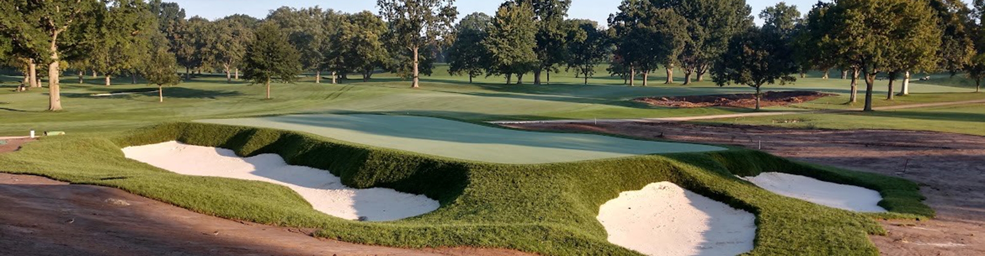 Golf course with sand bunkers and trees in the background at sunset