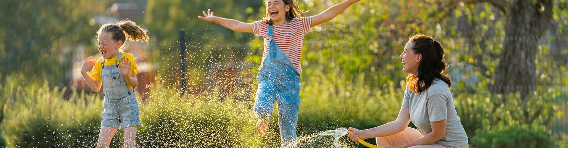 Women with two children playing in grass with watering hose