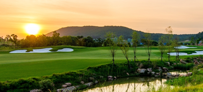Golf course with a hill and setting sun in background