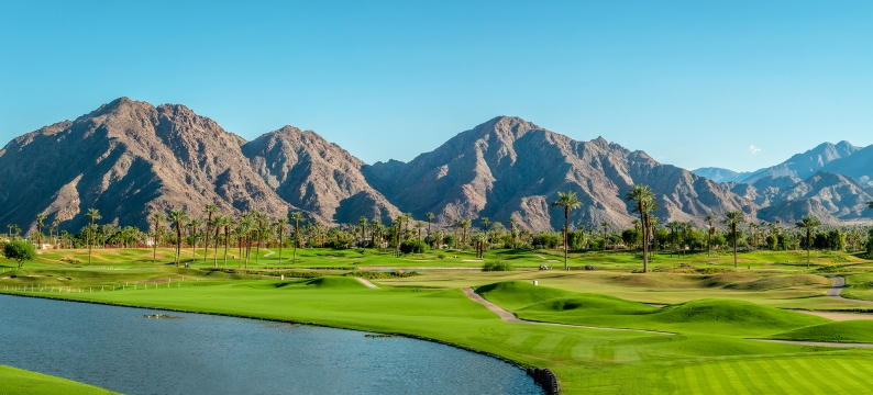 Golf course with green grass, palm trees, cliffs in background