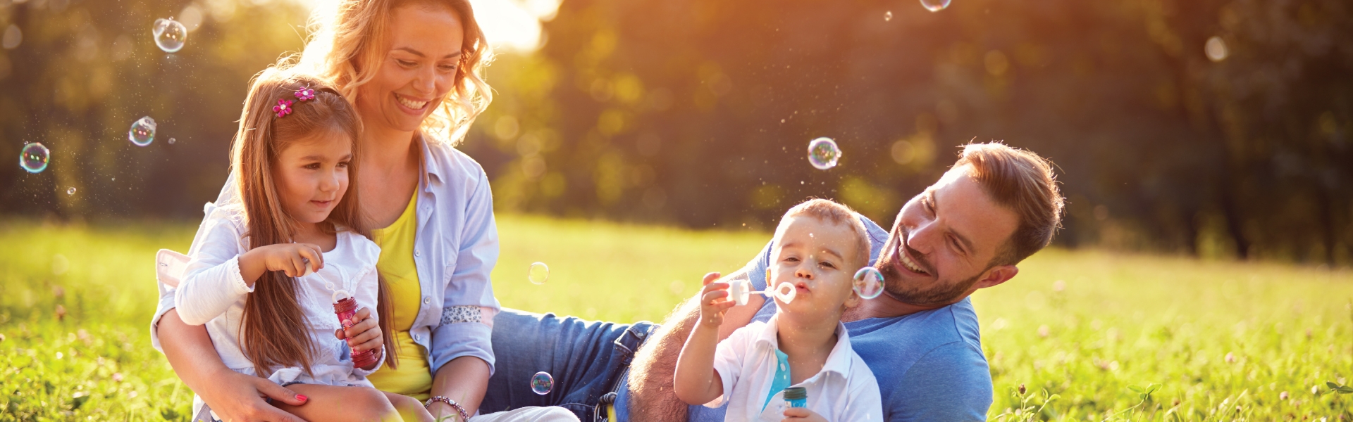 Family blowing bubbles in home lawn on sunny day.