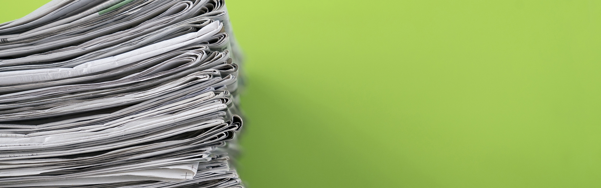 Stack of newspapers against a lime green wall 