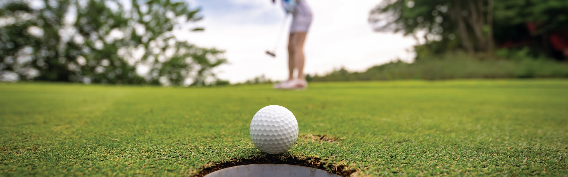 Female putting white golf ball into hole on putting green.