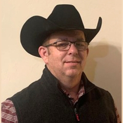 Headshot of a man in a black cowboy hat and a black vest with red and white shirt. 